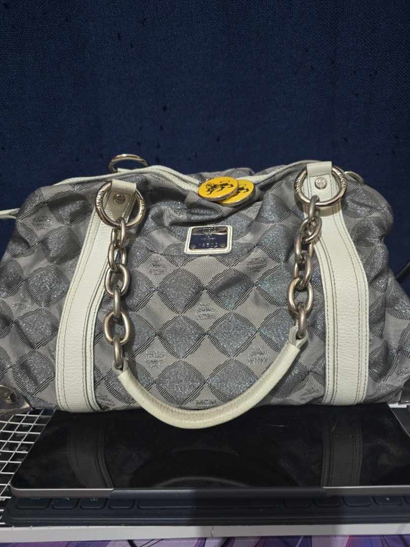 MCM Silver Handbag with Chain Detail (Category: Luxury Bags & Wallets) located in Manila. Submitted by heartless724 (Listing ID 1434524050, Image 1). Description: - Stylish MCM handbag - Silver with white accents - Diamond pattern design - Chain details - White leather base - Zipper closure - Two yellow circular charms - Silver hardware - Structured shape.