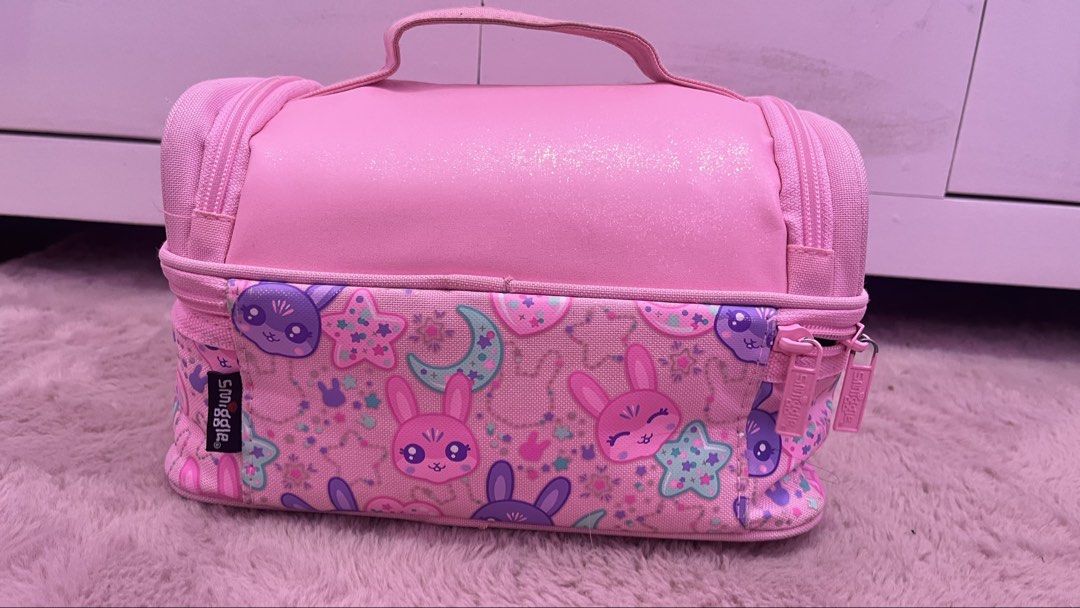 Smiggle Pink Bunny Lunch Bag (Category: Other Babies Going Out Needs) located in Tarlac. Submitted by jiegie (Listing ID 1434441171, Image 2). Description: - Smiggle lunch bag with a pink bunny design. - Two compartments for separating food and drinks. - Insulated interior to keep food fresh. - Includes a handle for easy carrying. - Features a name tag. - Pink color with bunny and star pattern on the bottom compartment. - Secure zipper closure..