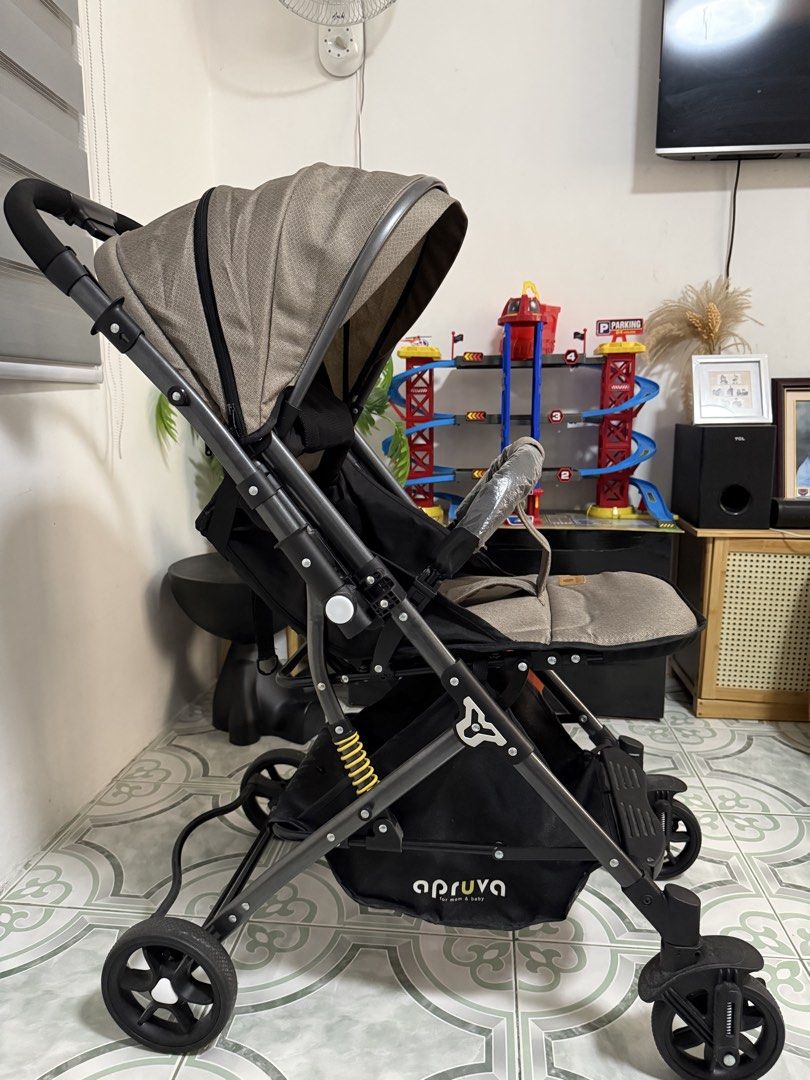Apruva Stroller (Category: Strollers) located in Pililla. Submitted by sim2fast (Listing ID 1434703793, Image 2). Description: Apruva stroller features a beige and black color scheme. It has a sunshade, a safety bar, and a storage basket underneath. The stroller has a five-point harness for safety. The wheels are black and the frame is dark gray..