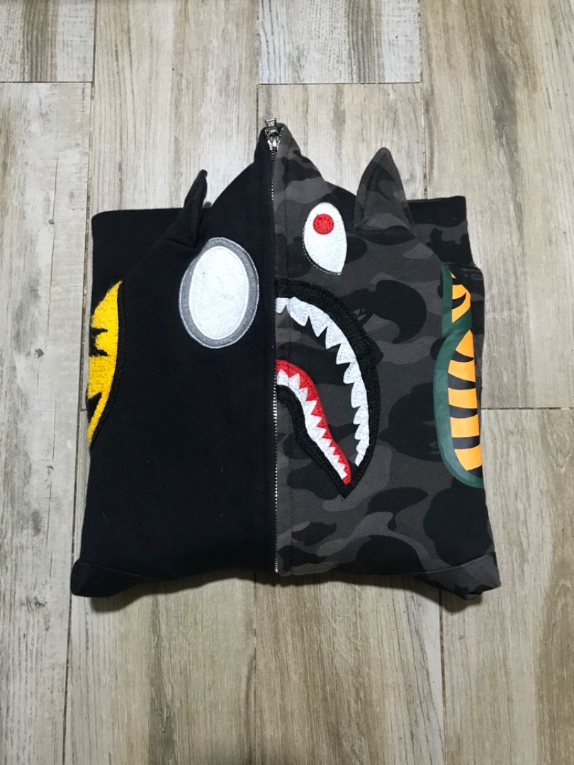 BAPE Batman Shark Hoodie (Category: Coats, Jackets and Outerwear) located in Manila. Submitted by timiasunci72128 (Listing ID 1434785351, Image 1). Description: BAPE hoodie features a unique split design with a Batman logo on one side and a shark face on the other. It has a full zip closure and a hood with ears. The hoodie showcases a camouflage pattern on the shark side and a yellow Batman logo. The DC logo is visible on the sleeve..