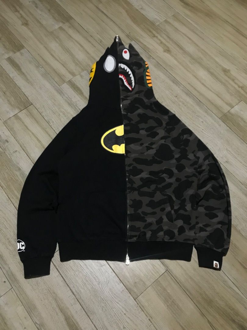 BAPE Batman Shark Hoodie (Category: Coats, Jackets and Outerwear) located in Manila. Submitted by timiasunci72128 (Listing ID 1434785351, Image 2). Description: BAPE hoodie features a unique split design with a Batman logo on one side and a shark face on the other. It has a full zip closure and a hood with ears. The hoodie showcases a camouflage pattern on the shark side and a yellow Batman logo. The DC logo is visible on the sleeve..