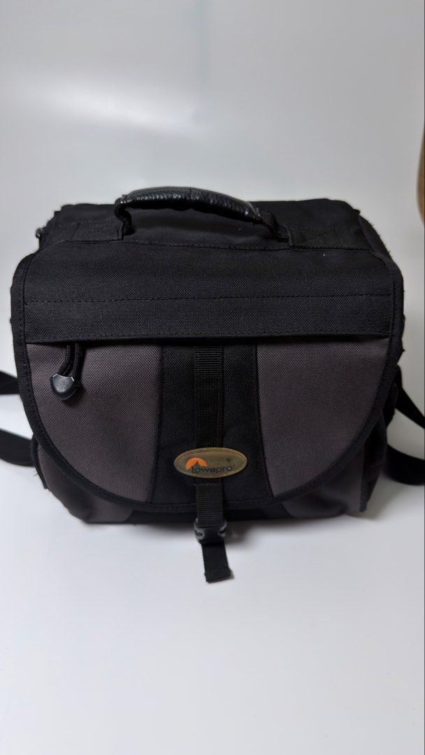 Lowepro EX 180 Camera Bag (Category: Camera Bags & Carriers) located in Alfonso. Submitted by jbcamet (Listing ID 1434732297, Image 2). Description: Lowepro EX 180 camera bag features a black and gray design with a shoulder strap and a top handle. It has a main compartment with adjustable dividers and a front pocket. The bag has the Lowepro logo on the front and the model name on the side. It also has a mesh side pocket and a buckle closure..