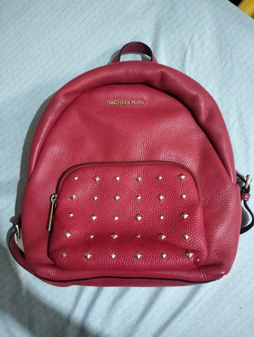Michael Kors Red Studded Backpack (Category: Backpacks) located in Laoag. Submitted by loml_e.zt (Listing ID 1434802674, Image 1). Description: - Authentic Michael Kors backpack - Vibrant red color - Gold-colored stud details on front pocket - Top handle and adjustable straps - Zipper closure - Main compartment and interior pocket - Michael Kors logo visible.
