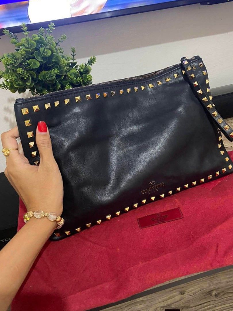 Valentino Garavani Rockstud Clutch (Category: Luxury Bags & Wallets) located in Manila. Submitted by ms.aaiyah07 (Listing ID 1434603308, Image 1). Description: Authentic Valentino Garavani Rockstud clutch bag. Black leather with gold-tone studs. Features zip closure, wrist strap, and red interior label. Includes dust bag. has signed of use but still in good condition.