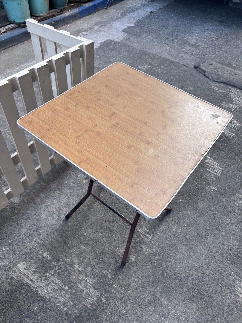 Folding Outdoor Square Table with Wooden Top (Category: Tables & Sets) located in Manila. Submitted by offtherack_mnl (Listing ID 1434869687, Image 3). Description: - Square folding table - Wooden-look top - Metal frame and legs - White trim on edges - Ideal as a side table or small dining table - Folds for convenient storage - 24” x 24” x 31”.