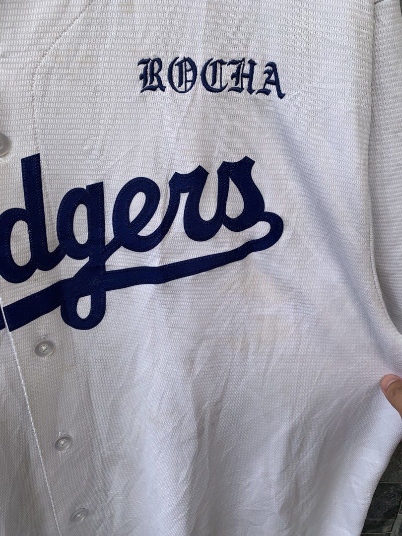 Nike Los Angeles Dodgers Baseball Jersey (Category: Tshirts & Polo Shirts ) located in Manila. Submitted by gelove.thrift (Listing ID 1434808202, Image 3). Description: - Authentic Nike Los Angeles Dodgers baseball jersey - Features the Dodgers logo and "ROCHA" on the front - Made with breathable, textured fabric - Includes Nike and MLB logos - Button-up front and short sleeves - Size tag is visible - Minor tear on the side.