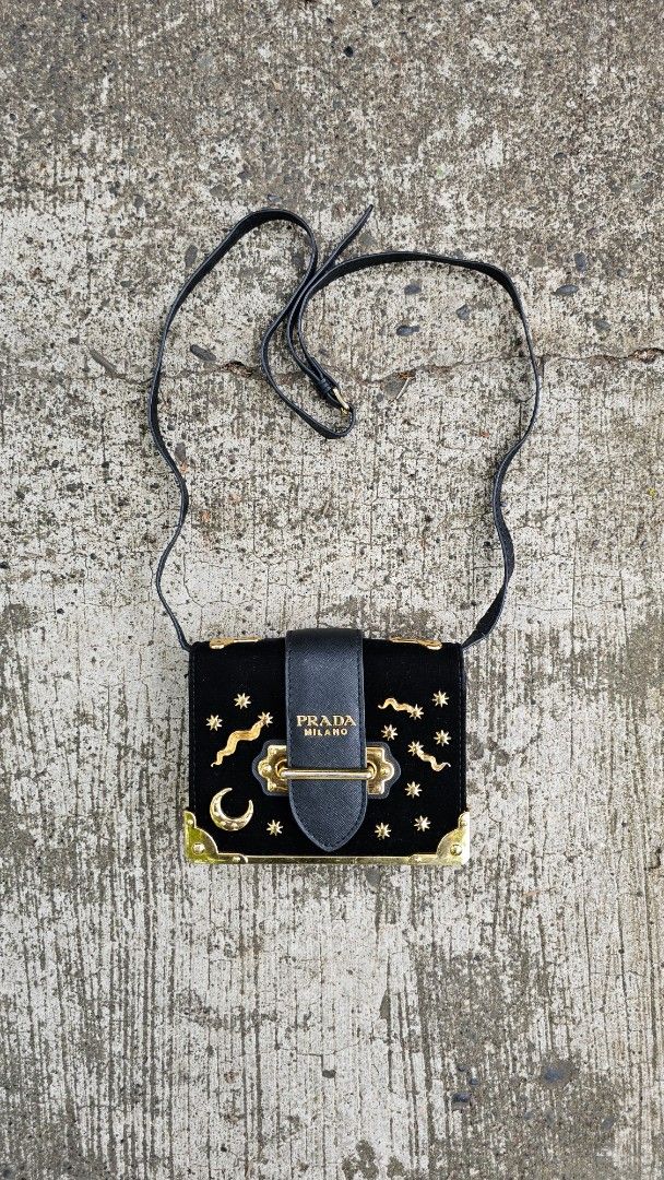 Prada Milano Celestial Crossbody Bag (Category: Luxury Bags & Wallets) located in Kibawe. Submitted by Thrift_ni_Babac (Listing ID 1434955986, Image 1). Description: - Prada Milano crossbody bag - Black velvet exterior with gold stars and accents - Black leather strap - Secure flap closure with Prada Milano logo - Black leather interior with a small compartment - Gold-toned hardware - Long strap for shoulder or crossbody wear (See last photo).
