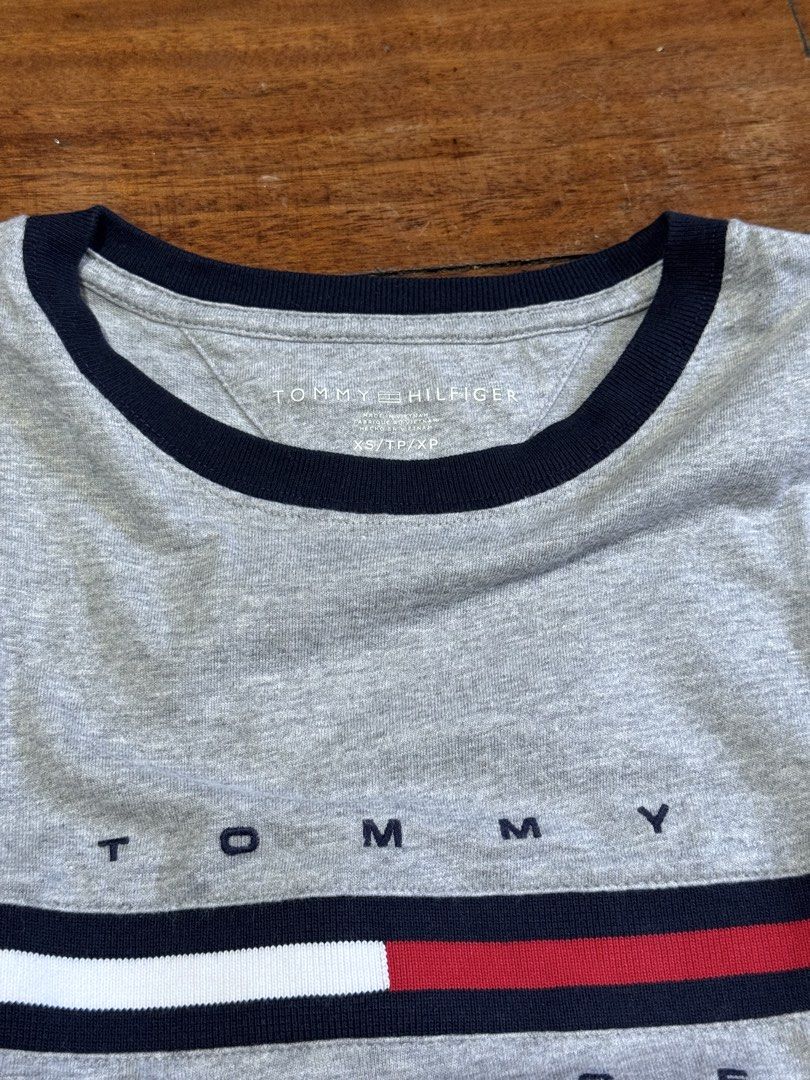 Tommy Hilfiger Gray T-shirt (Category: Tshirts & Polo Shirts ) located in Quezon City. Submitted by lilac8267 (Listing ID 1434857202, Image 2). Description: - Tommy Hilfiger T-shirt - Size: XS/XP - Color: Gray - Design: Navy blue neckline and chest stripe - Features the Tommy Hilfiger logo in white, red, and navy blue - Style: Crew neck.