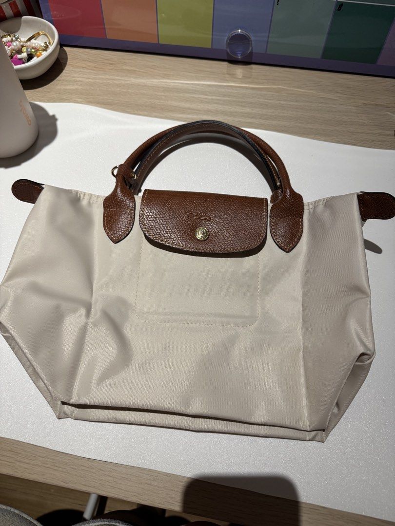 Longchamp Le Pliage Top Handle Bag (Category: Luxury Bags & Wallets) located in Quezon City. Submitted by mommashi (Listing ID 1435105165, Image 2). Description: - Authentic Longchamp Le Pliage top handle bag - color: Paper - Brown leather accents - Top flap with snap closure - Top handle - Includes dust bag - Minor stain on the side see pictures.