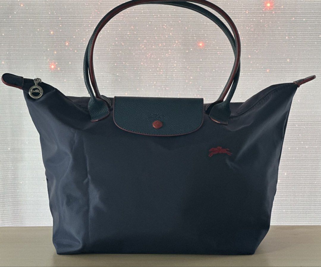 Longchamp Le Pliage Tote Bag - Navy (Category: Luxury Bags & Wallets) located in Midsayap. Submitted by bagski (Listing ID 1435168788, Image 1). Description: - Navy Longchamp Le Pliage tote bag - Flap closure with snap button - Dark green leather accents and handles with red trim - Includes a small silver charm - Longchamp logo visible - Classic and stylish design.