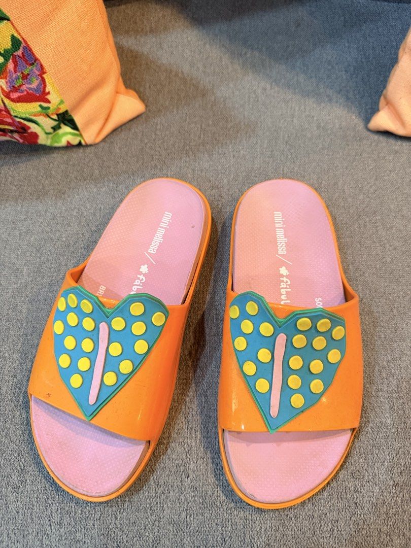 Mini Melissa Heart Slides US 3 (Teens) (Category: Babies & Kids Fashion) located in Tagum. Submitted by katecullin13 (Listing ID 1435053502, Image 2). Description: - Mini Melissa slides - Vibrant orange and pink color - Features a heart design - Comfortable slide-on style - Perfect for casual wear - Made of durable material - Heart-shaped embellishment with yellow dots and blue outline.