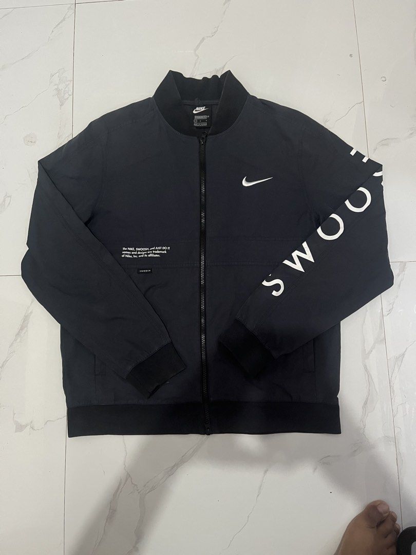 Nike Swoosh Bomber Jacket - Black - Size L (Category: Coats, Jackets and Outerwear) located in Manila. Submitted by madebyph (Listing ID 1435125291, Image 1). Description: Black Nike bomber jacket with white Swoosh logo and "SWOOSH" printed on the sleeves. Features a full-zip closure and a ribbed collar and cuffs. The back of the jacket has a large Swoosh logo and "NIKE SWOOSH JUST DO IT" printed. Made in Vietnam. Size L..