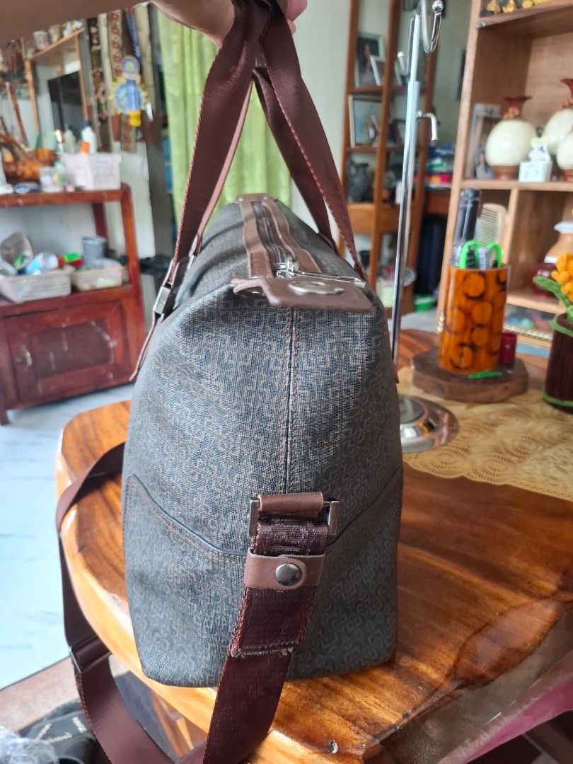 Goldlion Travel Bag (Category: Luxury Bags & Wallets) located in Libon. Submitted by jaladzarmi80045 (Listing ID 1429883249, Image 3). Description: Goldlion travel bag with a brown exterior and matching straps. Features a top handle and a detachable shoulder strap. Includes a front zipper pocket and a main compartment with an interior pocket. The bag has a patterned design and metal feet on the bottom. The brand name is visible on the bag and the