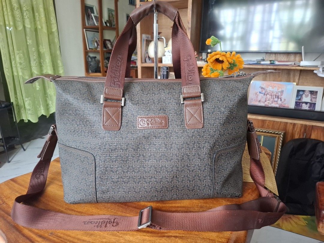 Goldlion Travel Bag (Category: Luxury Bags & Wallets) located in Libon. Submitted by jaladzarmi80045 (Listing ID 1429883249, Image 1). Description: Goldlion travel bag with a brown exterior and matching straps. Features a top handle and a detachable shoulder strap. Includes a front zipper pocket and a main compartment with an interior pocket. The bag has a patterned design and metal feet on the bottom. The brand name is visible on the bag and the