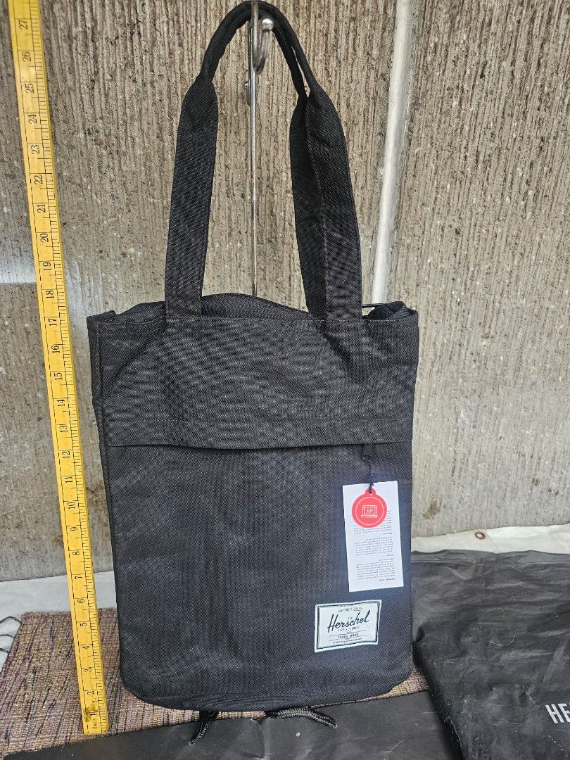 Herschel Supply Co. Tote Bag (Category: Laptop Bags & Sleeves) located in Manila. Submitted by onlinesmartshopping12 (Listing ID 1429906664, Image 3). Description: Herschel Supply Co. tote bag features a black exterior and a red and white striped interior. It has a front pocket and a zippered main compartment. The bag includes a tag indicating it can fit a 13-inch laptop. The bag has two handles for carrying..