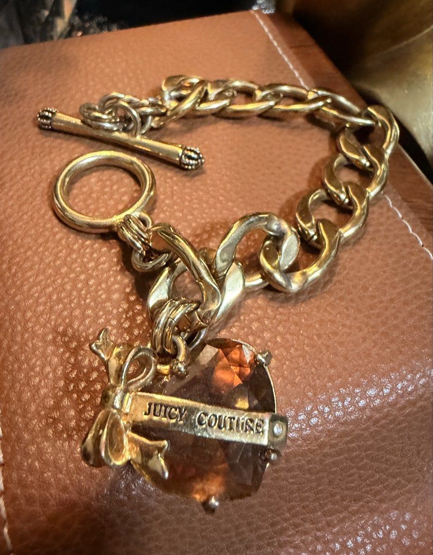 Juicy Couture Gold Charm Bracelet (Category: Bracelets) located in Marikina City. Submitted by landertroy (Listing ID 1430022743, Image 2). Description: Gold-toned bracelet features a chunky chain design and a toggle clasp. It includes a heart-shaped charm with the "Juicy Couture" logo. The charm has a faceted, amber-colored stone. The overall design is stylish and eye-catching. Small to medium size..