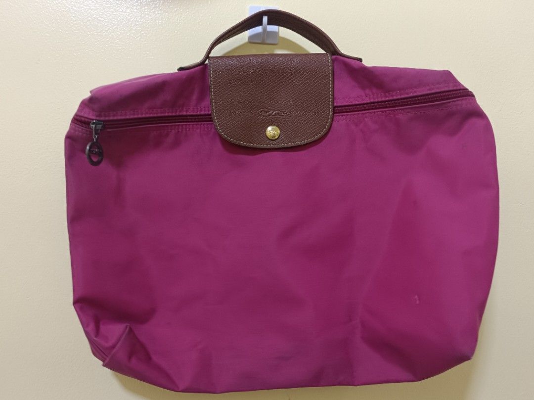 Longchamp Le Pliage Travel Bag (Category: Luxury Bags & Wallets) located in Trece Martires City. Submitted by declutterbyedi (Listing ID 1429982875, Image 1). Description: Authentic Longchamp Le Pliage travel bag in a vibrant magenta color. Features a brown leather flap with a gold-tone snap closure and handle. The bag has a zipper closure and a Longchamp logo charm. From Switzerland, needs bag cleaning..