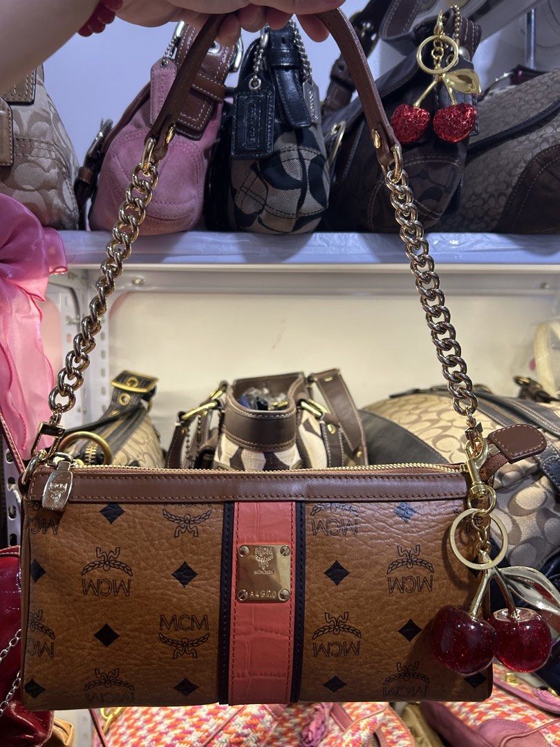 MCM Shoulder Bag with Chain (Category: Luxury Bags & Wallets) located in Manila. Submitted by graceyabut0 (Listing ID 1429949542, Image 1). Description: MCM shoulder bag features a brown monogram pattern with a pink stripe detail. It has a gold chain strap and a cherry charm. The interior includes multiple compartments and a zippered pocket. The bag is marked "Made in Korea" and has the MCM logo inside. The bag has a gold zipper and a gold MCM lo