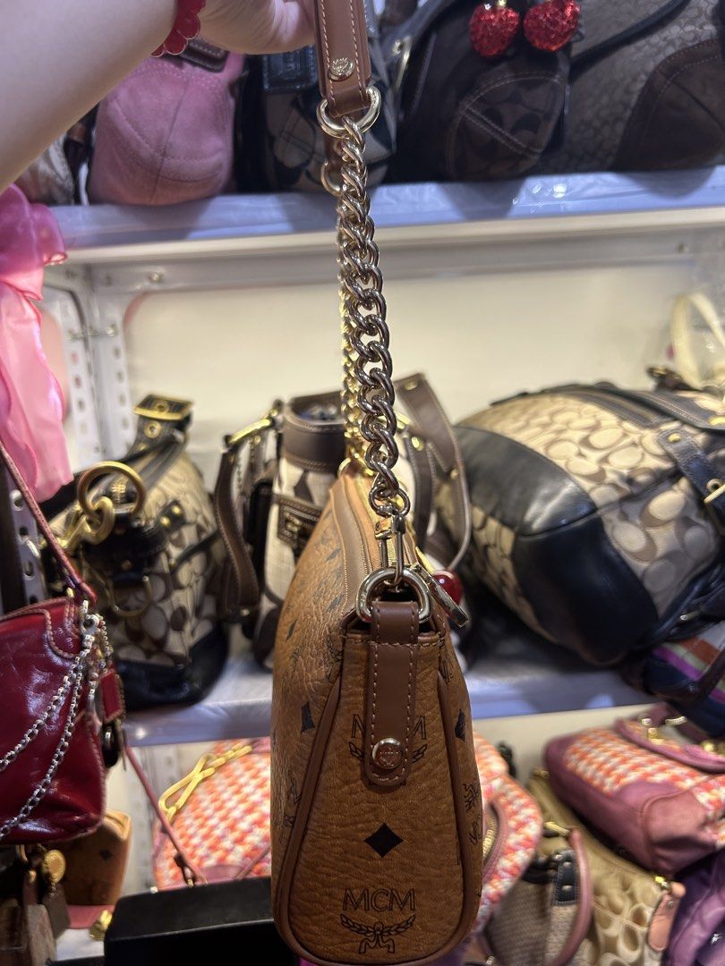 MCM Shoulder Bag with Chain (Category: Luxury Bags & Wallets) located in Manila. Submitted by graceyabut0 (Listing ID 1429949542, Image 3). Description: MCM shoulder bag features a brown monogram pattern with a pink stripe detail. It has a gold chain strap and a cherry charm. The interior includes multiple compartments and a zippered pocket. The bag is marked "Made in Korea" and has the MCM logo inside. The bag has a gold zipper and a gold MCM lo