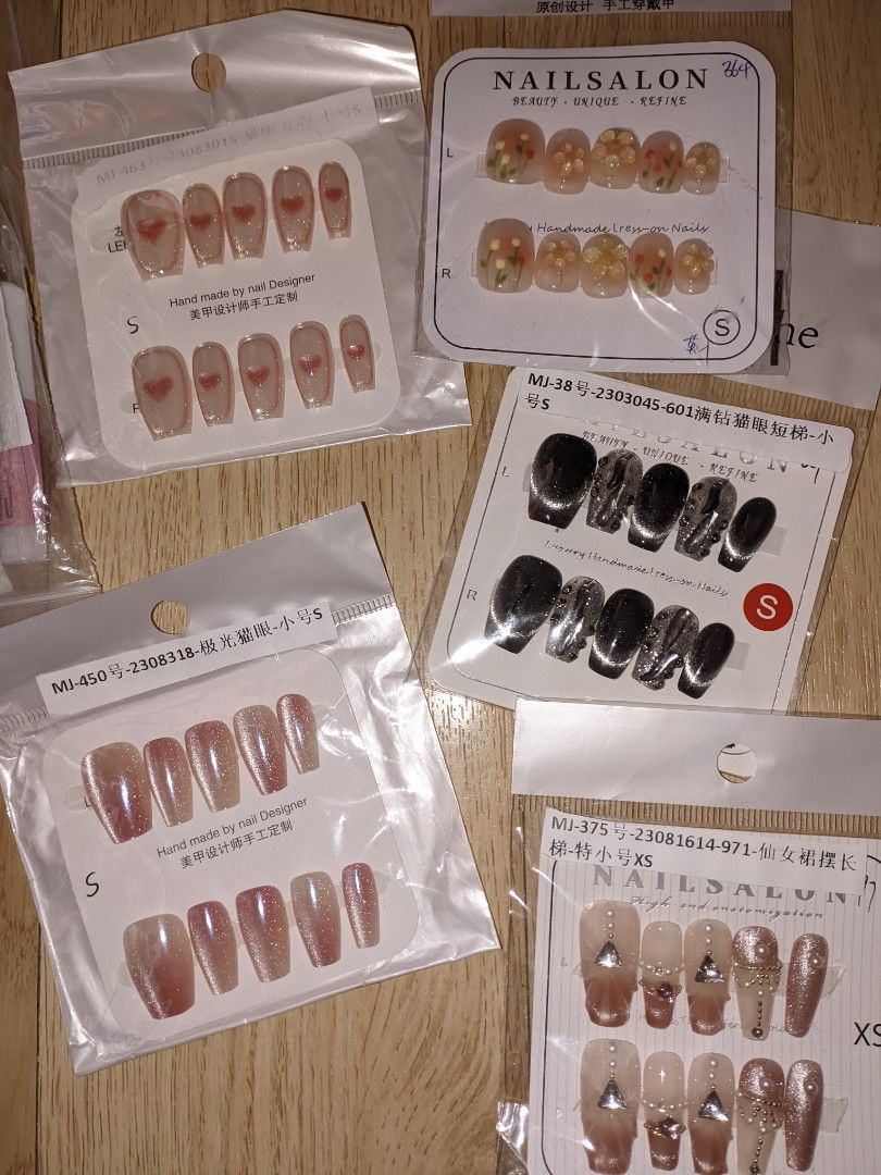 Premium Handmade Nail Art Press-on Nails Set (Category: Hands & Nails) located in Pasig City. Submitted by pottyhead.22 (Listing ID 1429990525, Image 2). Description: Set of premium press-on nails in various designs and sizes. Includes sets with heart designs, floral accents, and glitter effects. Available in sizes S and XS. Each set comes with multiple nails for a complete manicure. Designs include a mix of solid colors and patterned nails. ₱250