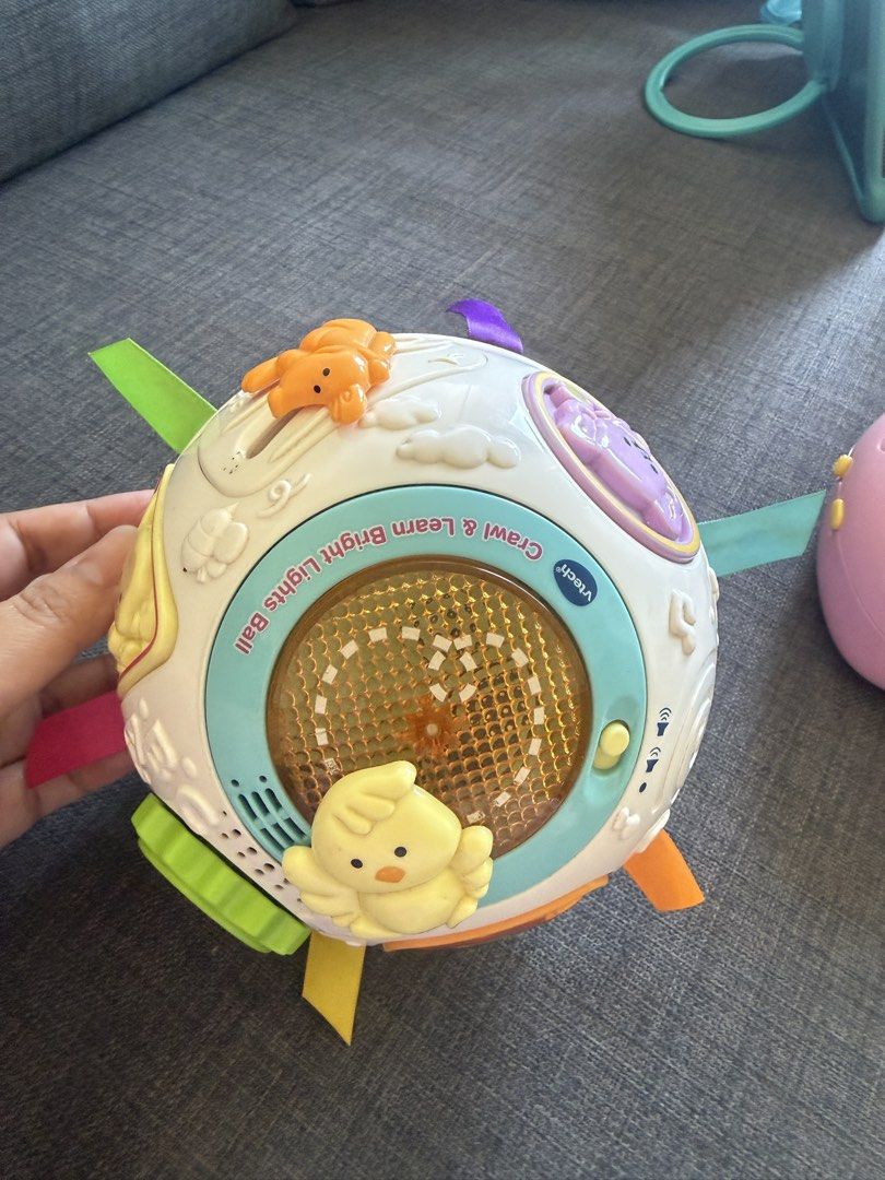 VTech Crawl & Learn Lights Ball & Lullaby Teddy Projector (Category: Infant Playtime) located in Mandaluyong City. Submitted by girlboss01 (Listing ID 1429881825, Image 2). Description: Listing includes two VTech baby toys. One is a Crawl & Learn Lights Ball with colorful ribbons and animal figures. The other is a Lullaby Teddy Projector, designed in pink with a teddy bear design. Both toys are designed for babies and toddlers. The projector has 