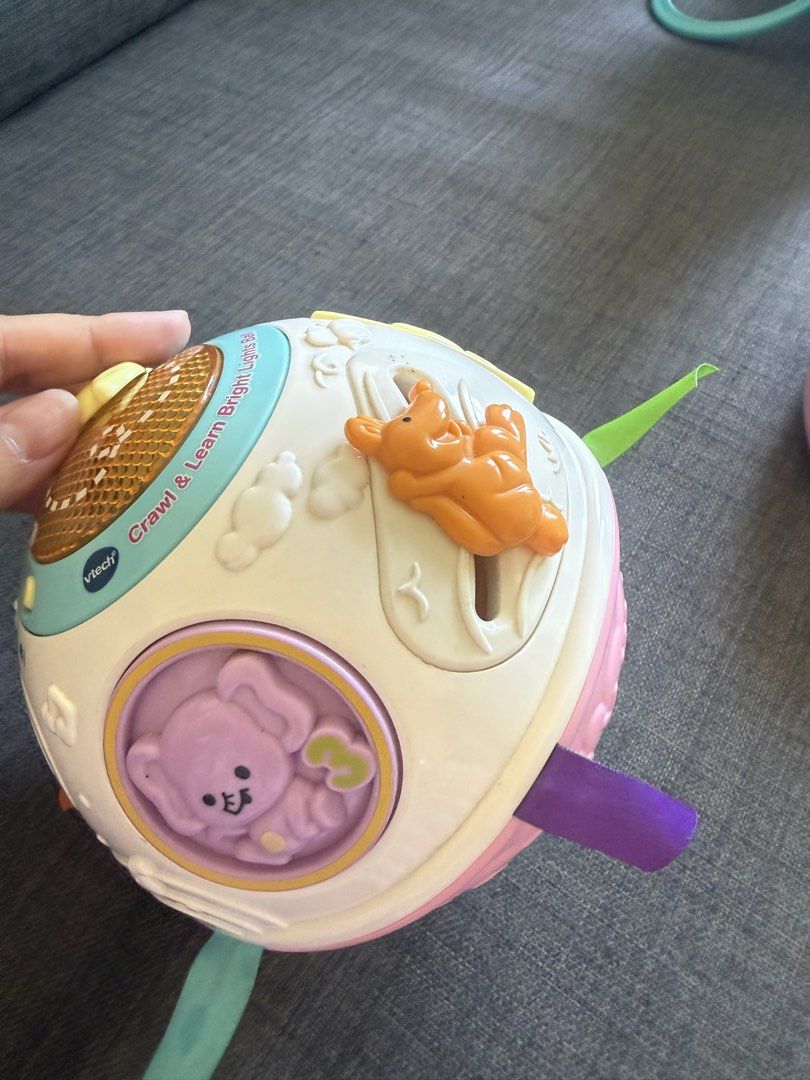VTech Crawl & Learn Lights Ball & Lullaby Teddy Projector (Category: Infant Playtime) located in Mandaluyong City. Submitted by girlboss01 (Listing ID 1429881825, Image 3). Description: Listing includes two VTech baby toys. One is a Crawl & Learn Lights Ball with colorful ribbons and animal figures. The other is a Lullaby Teddy Projector, designed in pink with a teddy bear design. Both toys are designed for babies and toddlers. The projector has 