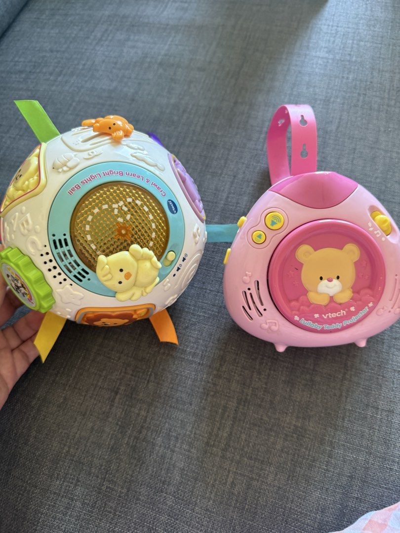 VTech Crawl & Learn Lights Ball & Lullaby Teddy Projector (Category: Infant Playtime) located in Mandaluyong City. Submitted by girlboss01 (Listing ID 1429881825, Image 1). Description: Listing includes two VTech baby toys. One is a Crawl & Learn Lights Ball with colorful ribbons and animal figures. The other is a Lullaby Teddy Projector, designed in pink with a teddy bear design. Both toys are designed for babies and toddlers. The projector has 