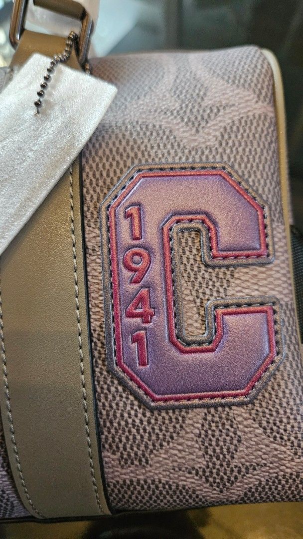 Coach Signature Handbag (Category: Other Accessories) located in Rizal. Submitted by vanbdc24 (Listing ID 1435250468, Image 3). Description: - Authentic Coach handbag - Signature pattern - Star detail - "1941" patch - Detachable strap - Top handle - Includes Coach paper bag - Color: Light brown and purple.