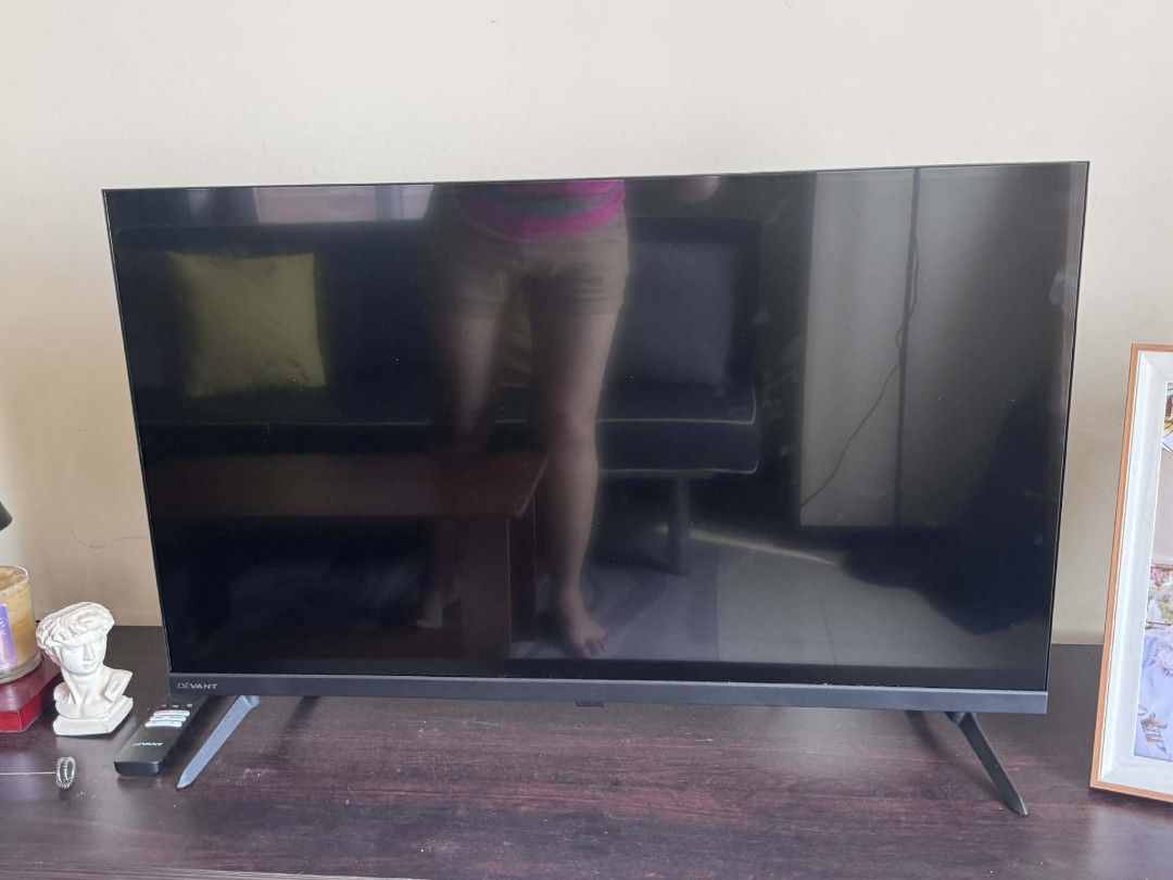 Devant LED TV (Category: TV) located in Manila. Submitted by jezm. (Listing ID 1430202538, Image 1). Description: Devant LED TV with a sleek black frame. It has a remote control and stands. The TV is placed on a wooden table. The screen is black, suggesting it is turned off. The legs are angled for stability..