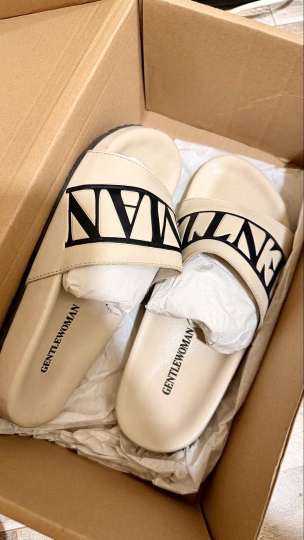 Gentlewoman Slides (Category: Slippers and slides) located in Manila. Submitted by authenticprelovedmnls (Listing ID 1430067239, Image 2). Description: Cream-colored slides from Gentlewoman. Features the brand name in black on the strap. The slides are placed on top of a Gentlewoman box. The footbed is a light cream color with the brand name printed on it. The slides appear to be new and unused. With box ..