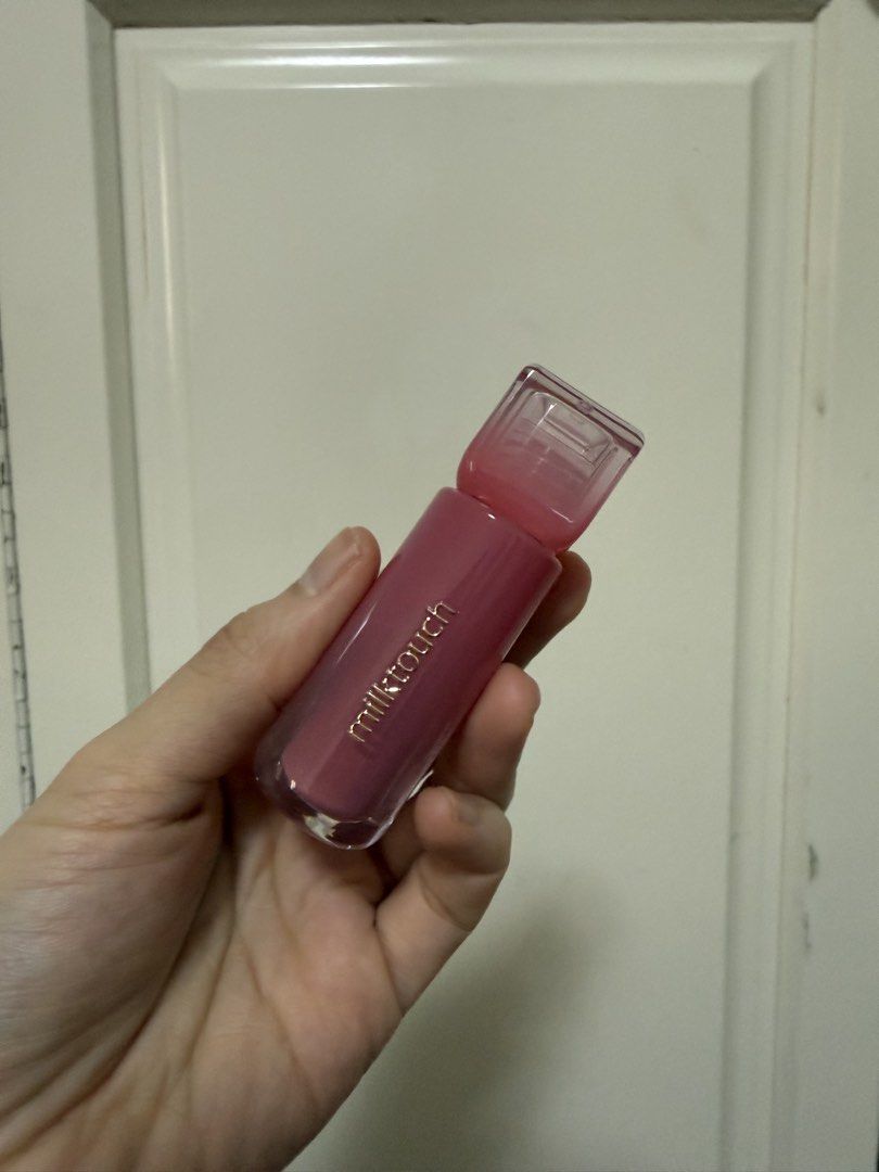 Milk Touch Be My Lip Tint - 03 (Category: Makeup) located in Manila. Submitted by maag16 (Listing ID 1430077735, Image 1). Description: Milk Touch Be My Lip Tint in shade 03. The lip tint is a pinkish-red color. The product is made in Korea. The packaging is a clear bottle with a slanted applicator. The brand name is printed in gold on the bottle..