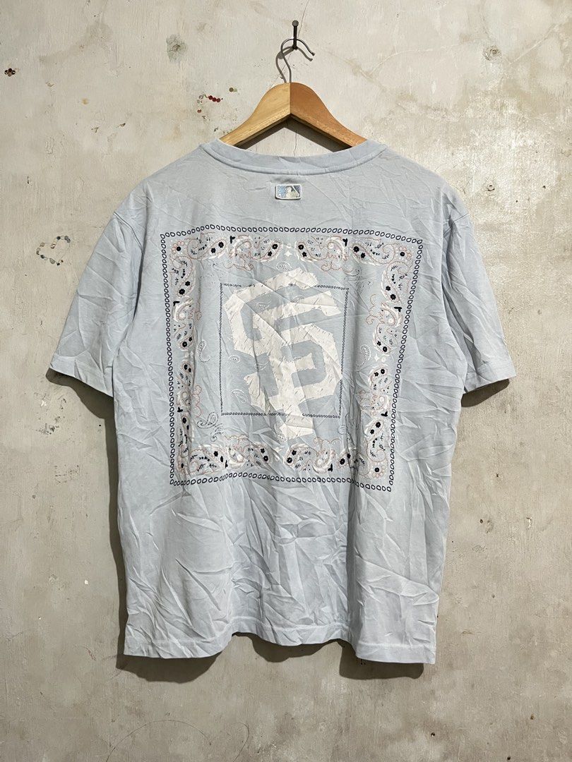 MLB San Francisco Giants T-shirt (Category: Tshirts & Polo Shirts ) located in Santa Cruz. Submitted by thriftgane0.2 (Listing ID 1430103953, Image 1). Description: Light blue MLB San Francisco Giants t-shirt. Features the SF logo on the front and back. The back has a large SF logo within a bandana-style design. The MLB logo is visible on the collar. The sleeve has the SF logo embroidered. Size M..