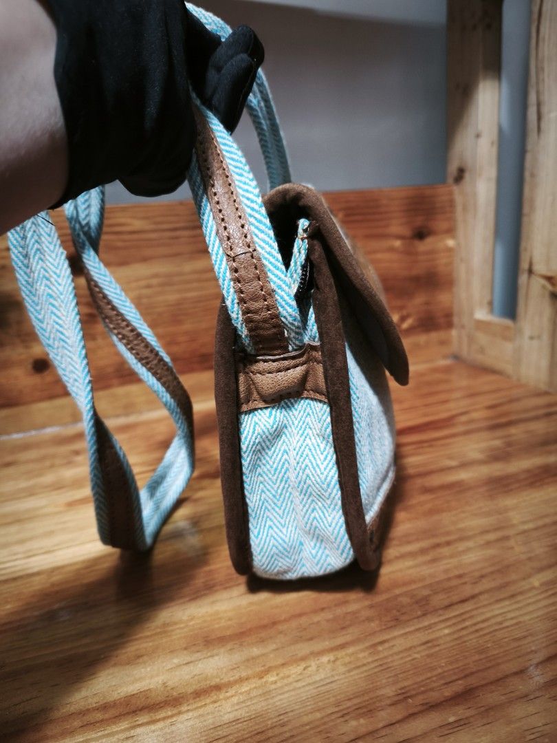 Nepal Handmade Crossbody Bag (Category: Cross-body Bags) located in Baguio. Submitted by queenlyne_vintage_rare_finds (Listing ID 1430032821, Image 3). Description: Crossbody bag features a unique design with a light blue herringbone pattern and brown leather accents. It has a flap closure with a round leather detail and a zippered pocket on the back. The bag includes an adjustable strap and a spacious interior. Measurements are approximately 8 i
