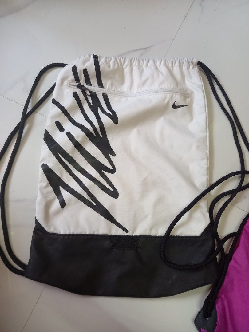 Nike Drawstring Bag (Category: Backpacks) located in Tuguegarao City. Submitted by zenphoenix-7ad615 (Listing ID 1430051724, Image 2). Description: Drawstring bag features a vibrant purple and black color scheme with the iconic Nike logo. It also has a white bag with a black design and a small zippered pocket. The bag is designed with drawstring closure for easy access and secure storage. Perfect for carrying your essentials in style. bundle of 2