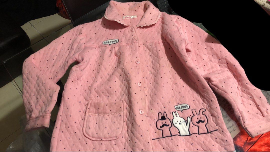 Pink Quilted Pajama Jacket with Cartoon Design (Category: Babies & Kids Fashion) located in Mandaluyong City. Submitted by jennyitems (Listing ID 1430210893, Image 1). Description: 👚 Pink pajama jacket features a quilted design with black polka dots. 🧥 It has a collar with lace trim, a button-up front, and two pockets. 🌸 The jacket is adorned with a "Bonjour" speech bubble and a cartoon bunny 🐰 🌸 The size tag indicates it is a size L. 🌸 So 
