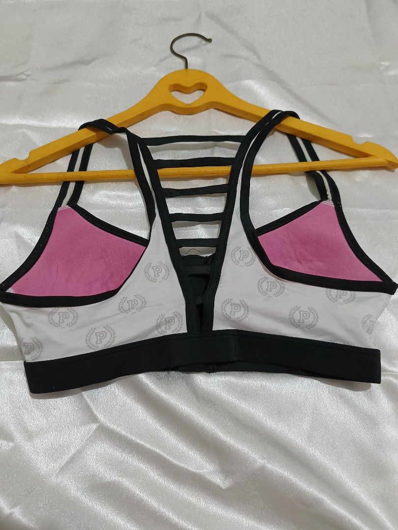 Pink Victoria's Secret Ultimate Sports Bra XS (Category: Activewear) located in Bago City. Submitted by cossacloset (Listing ID 1430053036, Image 2). Description: Pink Victoria's Secret Ultimate sports bra in size XS. Features a white base with the Pink logo pattern, black trim, and a zipper closure. The back has a strappy design with pink lining. The tag indic ates it is an Ultimate sports bra. The bra is designed for athletic activities. Prelov