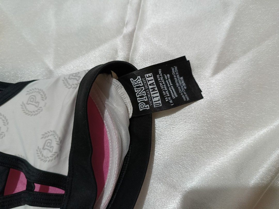 Pink Victoria's Secret Ultimate Sports Bra XS (Category: Activewear) located in Bago City. Submitted by cossacloset (Listing ID 1430053036, Image 3). Description: Pink Victoria's Secret Ultimate sports bra in size XS. Features a white base with the Pink logo pattern, black trim, and a zipper closure. The back has a strappy design with pink lining. The tag indic ates it is an Ultimate sports bra. The bra is designed for athletic activities. Prelov