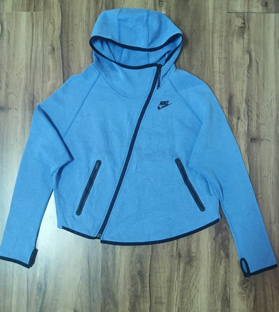 Nike Tech Fleece Hoodie Jacket XL (Category: Coats, Jackets and Outerwear) located in Bacoor. Submitted by toffs16 (Listing ID 1430214866, Image 1). Description: Nike Tech Fleece hoodie jacket in a light blue color. Features a unique diagonal zipper design, two front pockets, and a hood. The jacket has black accents along the zipper and pockets. The Nike logo is visible on the chest. Size XL..