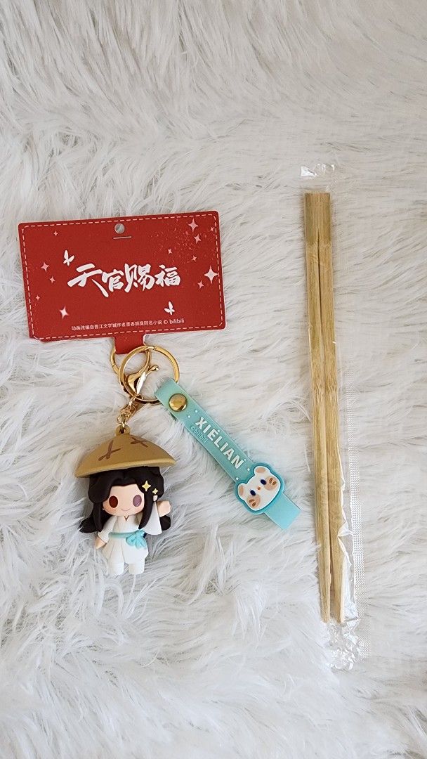 TGCF Xie Lian Keychain (Category: Character Goods) located in Manila. Submitted by quickocean (Listing ID 1430272995, Image 2). Description: Keychain features a character from Heaven Official's Blessing. It includes a figure of Xie Lian, a strap with the name "Xie Lian", and a red tag with Chinese characters. Also included are a pair of chopsticks. The keychain is attached to a gold-colored ring..