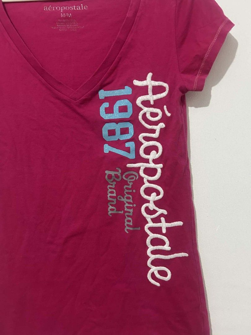Aéropostale V-neck T-shirt (Category: Shirts) located in Naga. Submitted by shiyaaah (Listing ID 1430781374, Image 2). Description: BODY HUGGING! Aéropostale V-neck T-shirt in pink. Features the brand name and "1987 Original Brand" printed on the front. The shirt has short sleeves and a V-neck design. The size is M/M. Tags: y2k, whimsy, whimsical, hollister, abercrombie, body hugging.