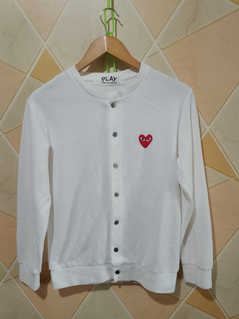 Play Comme des Garcons Knitted Cardigan (Category: Coats, Jackets and Outerwear) located in San Pedro. Submitted by jokwanrocks09 (Listing ID 1430793174, Image 1). Description: White cardigan from Play Comme des Garcons. Features the iconic red heart logo on the chest. It has a button-up front and long sleeves. The size is S. Made in Japan. The material is 100% cotton. The care label indicates hand wash only and no bleach. 19x24.5 small to medium