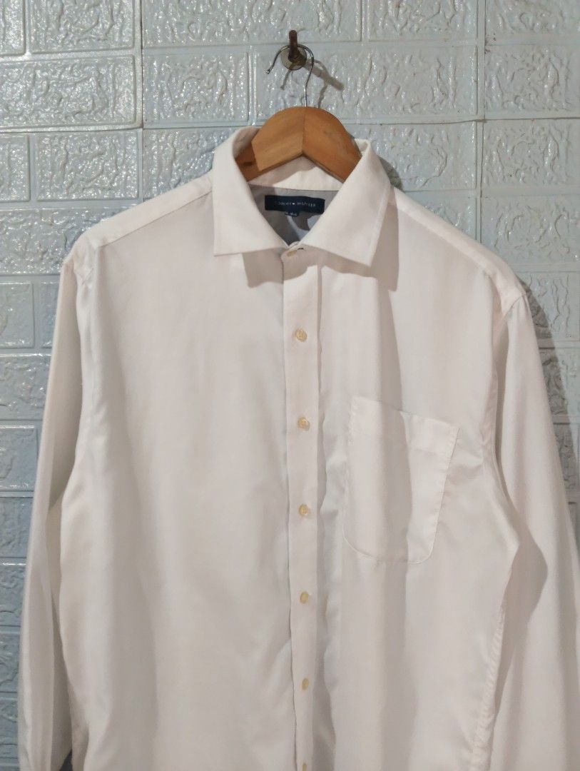 Tommy Hilfiger White Long Sleeve Shirt (Category: Tshirts & Polo Shirts ) located in Davao. Submitted by noelamihan05424 (Listing ID 1430659934, Image 2). Description: Classic white long sleeve shirt from Tommy Hilfiger. Features a button-down front, a chest pocket, and buttoned cuffs. The label indicates a size of 16-1/2 and a sleeve length of 32-33. Made in Bangladesh. Includes care instructions on the tag. Excellent to like new condition Authe