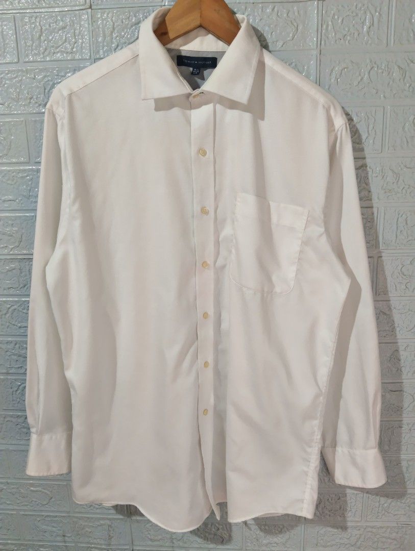Tommy Hilfiger White Long Sleeve Shirt (Category: Tshirts & Polo Shirts ) located in Davao. Submitted by noelamihan05424 (Listing ID 1430659934, Image 1). Description: Classic white long sleeve shirt from Tommy Hilfiger. Features a button-down front, a chest pocket, and buttoned cuffs. The label indicates a size of 16-1/2 and a sleeve length of 32-33. Made in Bangladesh. Includes care instructions on the tag. Excellent to like new condition Authe