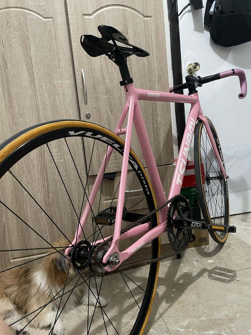 Tsunami SNM100 Fixed Gear Bike (Category: Bicycles) located in Paranaque City. Submitted by newhobbieshop (Listing ID 1430768910, Image 2). Description: Pink Tsunami SNM100 fixed gear bike. Features a black crankset, black handlebars, and a carbon fiber seat. Includes a pair of pedals. The bike has a pink frame and a black wheelset. The tires have a tan sidewall. The handlebars are wrapped in pink tape..
