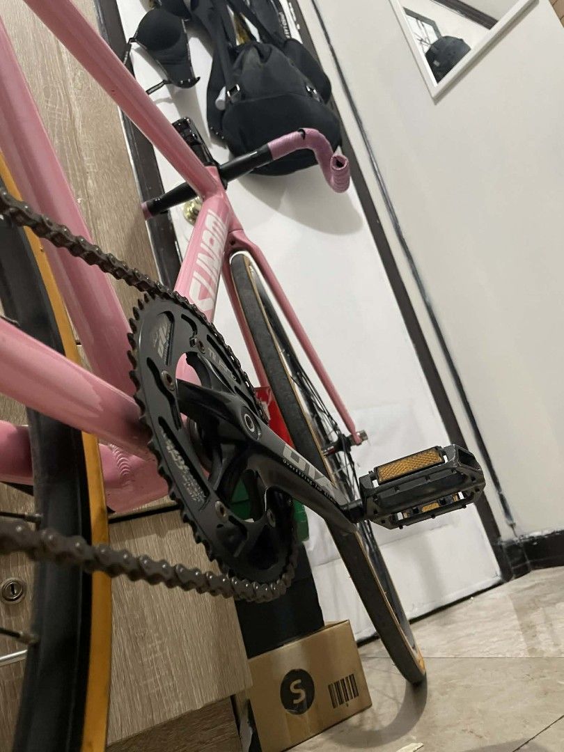 Tsunami SNM100 Fixed Gear Bike (Category: Bicycles) located in Paranaque City. Submitted by newhobbieshop (Listing ID 1430768910, Image 3). Description: Pink Tsunami SNM100 fixed gear bike. Features a black crankset, black handlebars, and a carbon fiber seat. Includes a pair of pedals. The bike has a pink frame and a black wheelset. The tires have a tan sidewall. The handlebars are wrapped in pink tape..