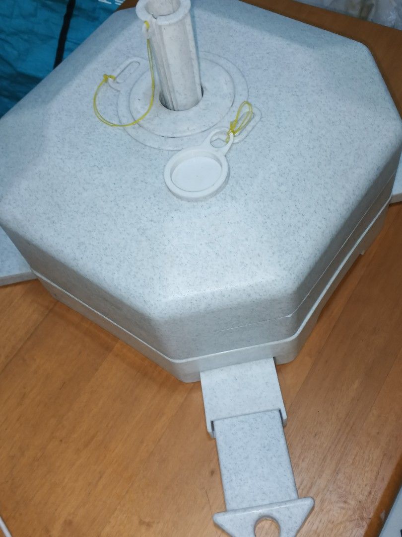 Umbrella Base (Category: Umbrellas) located in Caloocan City. Submitted by surplusandbnewshop (Listing ID 1430646827, Image 2). Description: - Sturdy umbrella base for outdoor use. - Octagonal design with four supporting legs for stability. - Includes a central pole holder and removable cap. - Made of a speckled, light-colored material. - Designed to securely hold a standard umbrella pole. - Easy to set up and use..