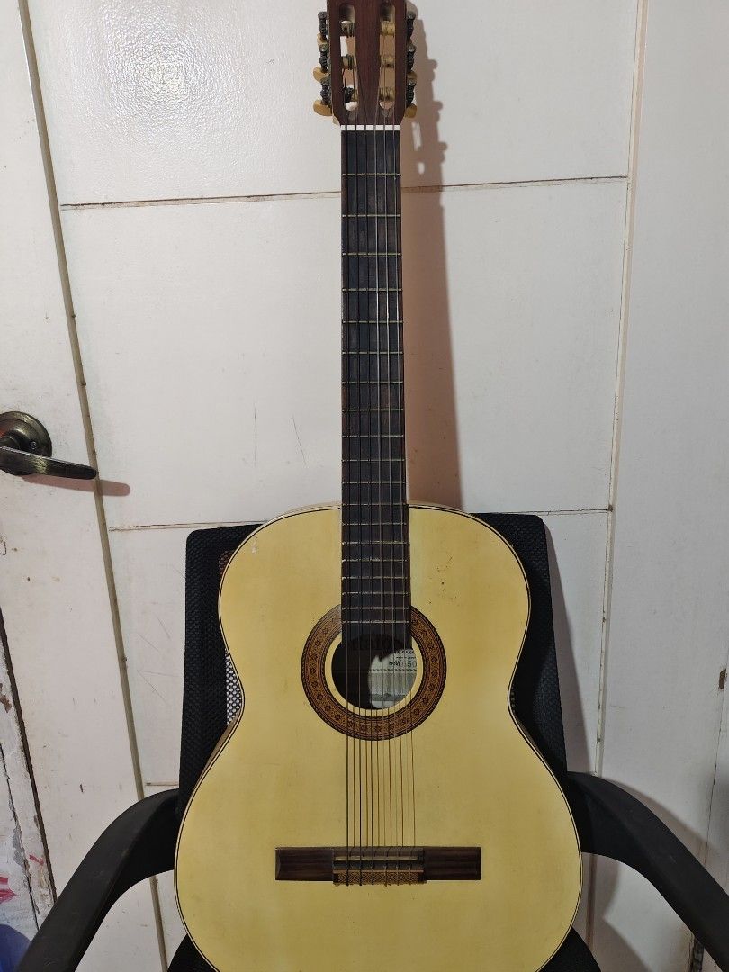 Classical Guitar (Category: Musical Instruments) located in Bulacan. Submitted by babz30261 (Listing ID 1430901193, Image 1). Description: Classical guitar with nylon strings. Features a light-colored body and a dark fretboard. The headstock has tuning pegs. The guitar is resting on a black chair. The body has a sound hole with decorative inlay. The back of the guitar is also light-colored..