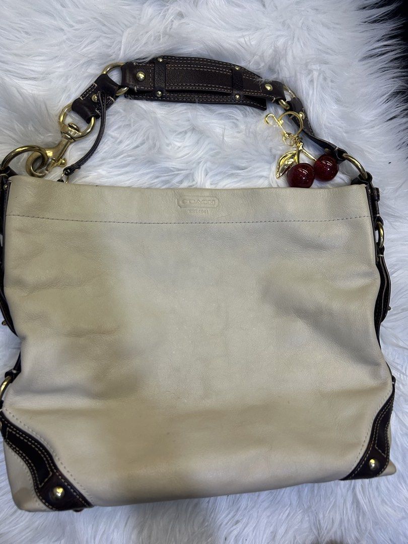 Coach Shoulder Bag with Cherry Charm (Category: Luxury Bags & Wallets) located in Manila. Submitted by graceyabut0 (Listing ID 1430890788, Image 1). Description: Coach shoulder bag with a light beige exterior and dark brown accents. Features gold-tone hardware and a cherry charm. The interior is lined with a light blue fabric. Includes a zip closure and a Coach tag with the serial number J0693-10616. The bag has a shoulder strap with a dark brown