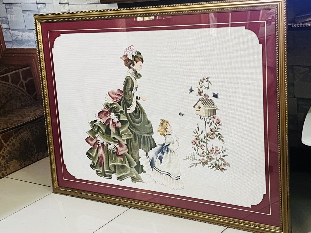 Framed Cross-stitch Embroidery (Category: Frames & Pictures) located in Antipolo. Submitted by murapod2 (Listing ID 1430820956, Image 3). Description: Beautifully framed cross-stitch embroidery featuring a Victorian-era woman and child. The artwork is set against a white background with a maroon border, encased in a gold-colored frame. The embroidery depicts a detailed scene with a birdhouse and floral accents. The piece is ready to hang and woul