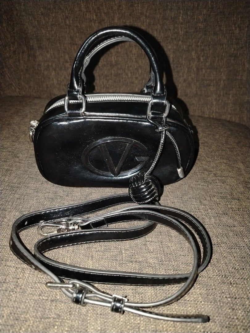Giovanni Valentino Black Handbag with Strap (Category: Luxury Bags & Wallets) located in Munoz. Submitted by makie_ukay (Listing ID 1430935568, Image 1). Description: Black handbag by Giovanni Valentino. Features a top handle and a detachable shoulder strap. The bag has a silver zipper and hardware. The interior is lined with a light-colored fabric and includes a small pocket. The exterior has a prominent "VG" logo. Includes a small decorative de